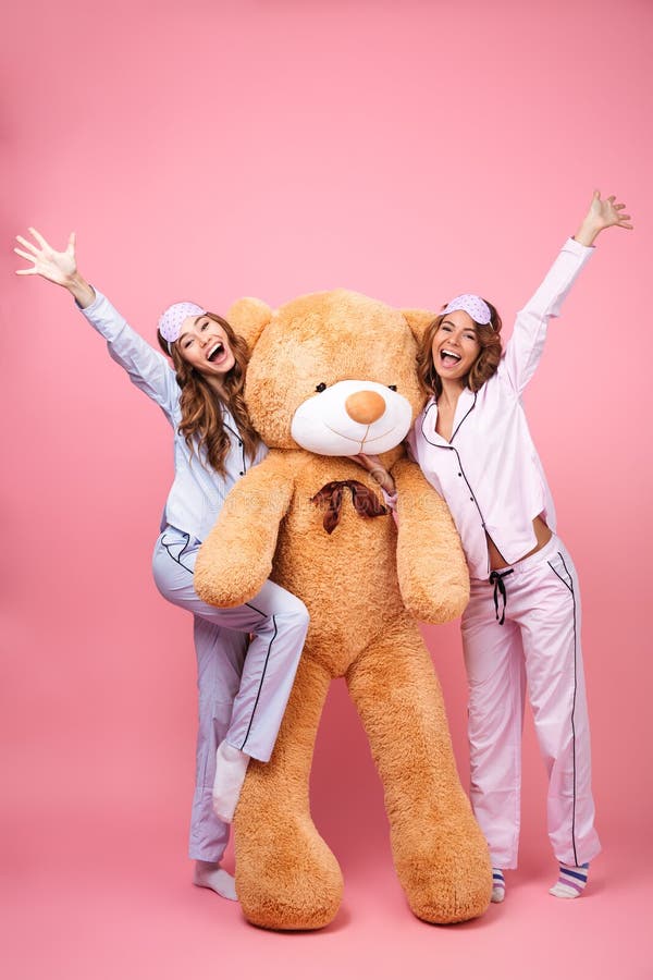 Cheerful friends women in pajamas hug big teddy toy bear. 