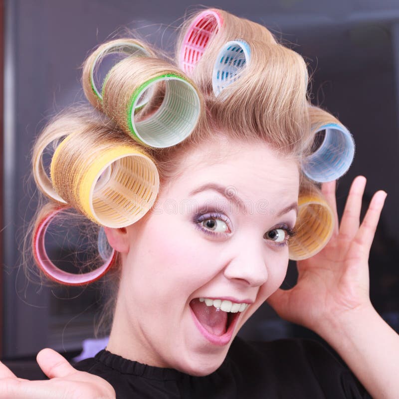 Cheerful funny blond girl hair curlers rollers by haidresser in beauty salo...