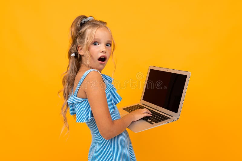 Cheerful girl in dress smiles with her laptop isolated on yellow and orange background