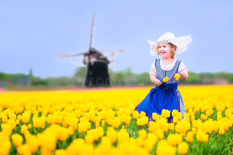 Cheerful girl in Dutch costume in tulips field with windmill