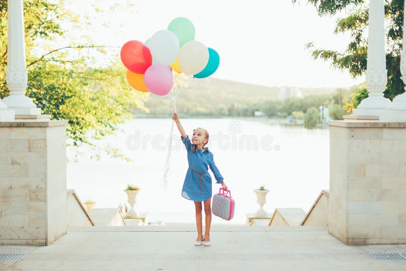 Cheerful girl holding colorful balloons and childish suitcase