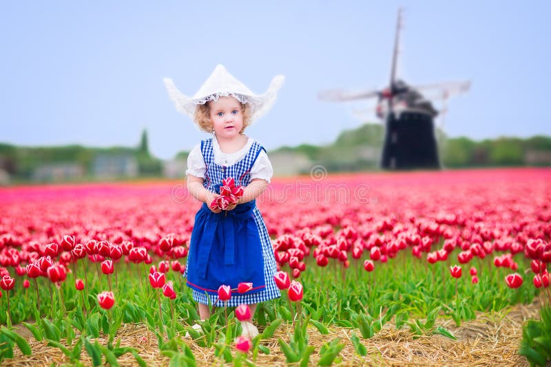 Cheerful girl in tulips field with windmill in Dutch costume