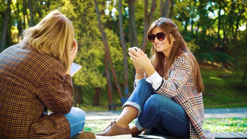 Cheerful girls sitting in park and browsing social media