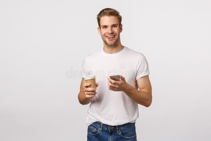 Cheerful good-looking modern blond man with bristle, holding paper cup of coffee, drinking tea and holding smartphone