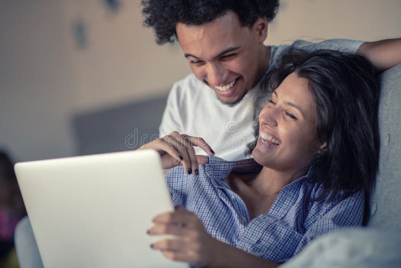 Cheerful happy African American young marriage laughing while watching movie on laptop computer at home interior, happy dark skinned couple in love shopping online on netbook enjoying store discounts. Cheerful happy African American young marriage laughing while watching movie on laptop computer at home interior, happy dark skinned couple in love shopping online on netbook enjoying store discounts