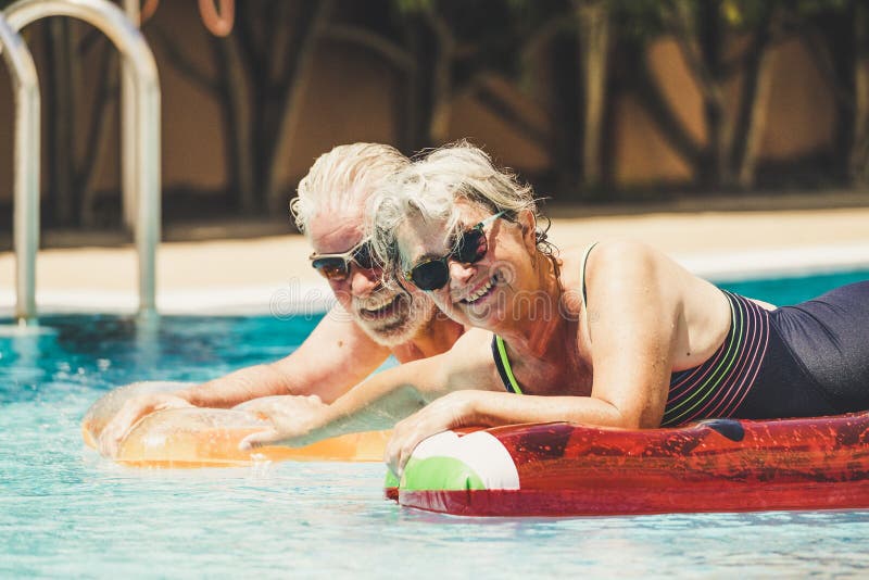 Cheerful happy coule of retired senior old people smile and enjoy together the pool in summer hoiday vacation with coloure trendy