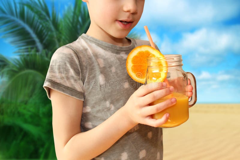 Cheerful kid, boy, holds a glass jar in his hand with orange juice from orange or lemon and drinks from a straw, the concept of a healthy diet, vitamins, lifestyle