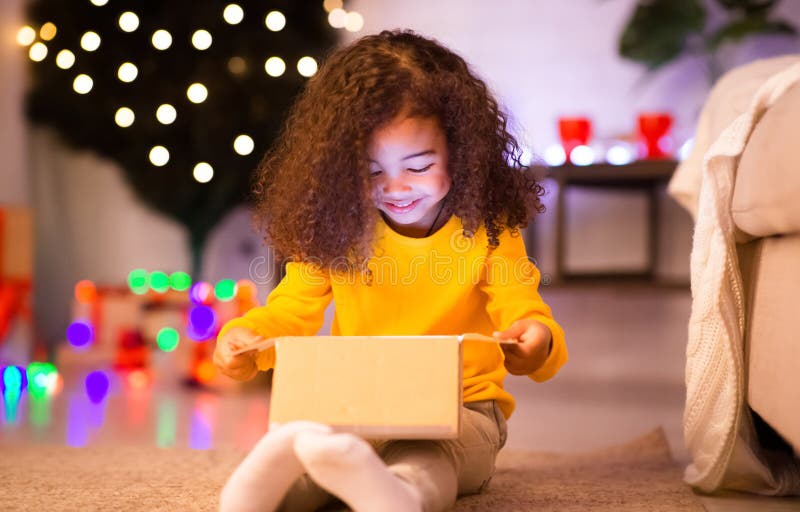 Cheerful, liten afrikansk tjej som öppnar julklapp från Santa royaltyfri fotografi
