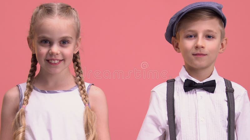 Cheerful little boy and girl looking into camera, isolated on pink background
