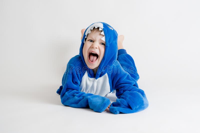 Cheerful little boy posing on a white background in pajamas, blue shark costume