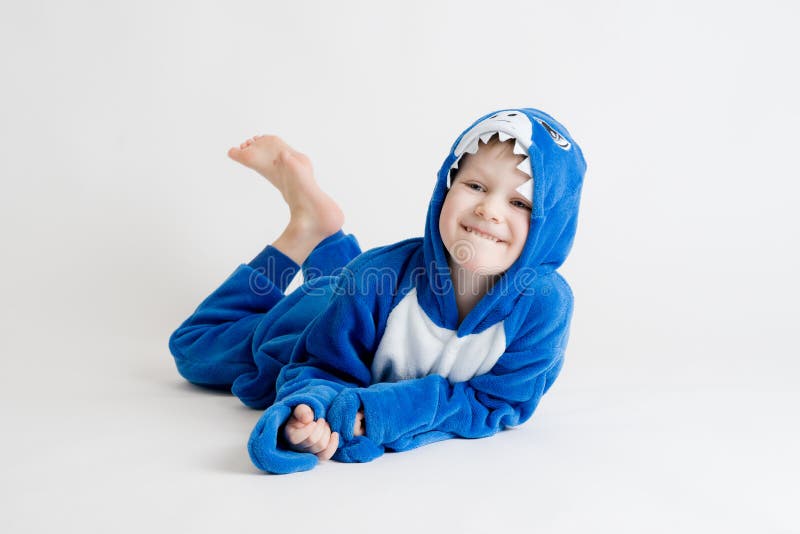 Cheerful little boy posing on a white background in pajamas, blue shark costume