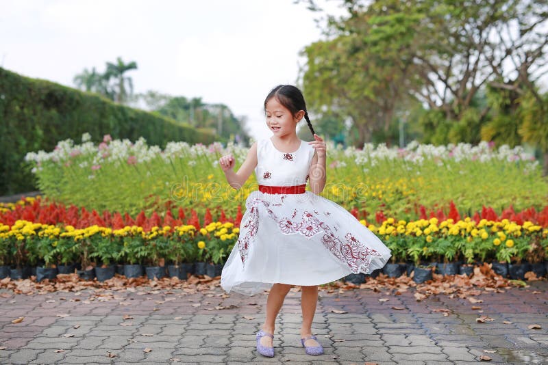 Cheerful little child girl dancing and having fun in the fresh flower garden. Kid play in the park outdoor