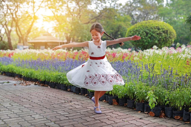 Cheerful little child girl dancing and having fun in the fresh flower garden. Kid play in the park outdoor