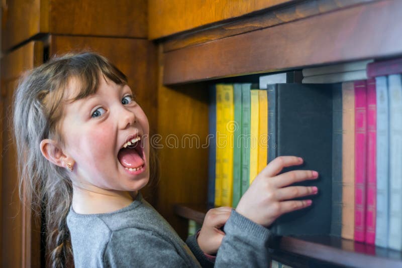 A Cheerful Little Girl Is Taking A Book From A Bookshelf Funny