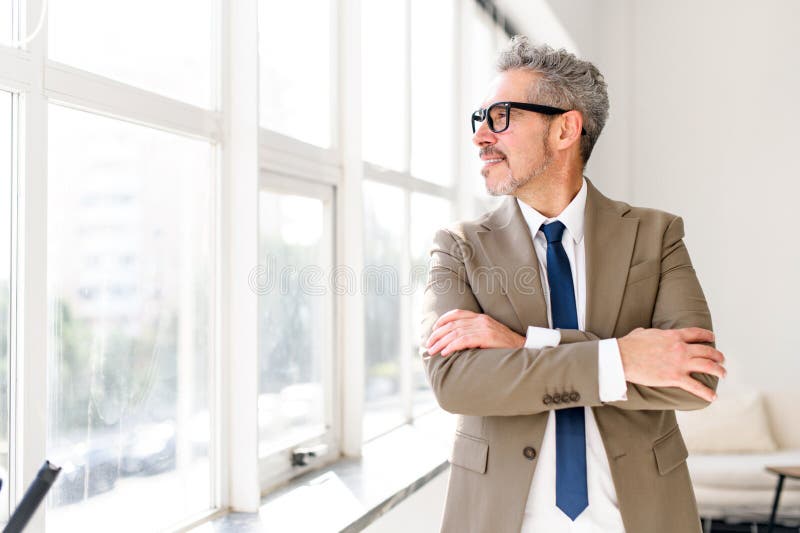 The cheerful mature grey-haired businessman looks off into the distance, arms crossed royalty free stock photo