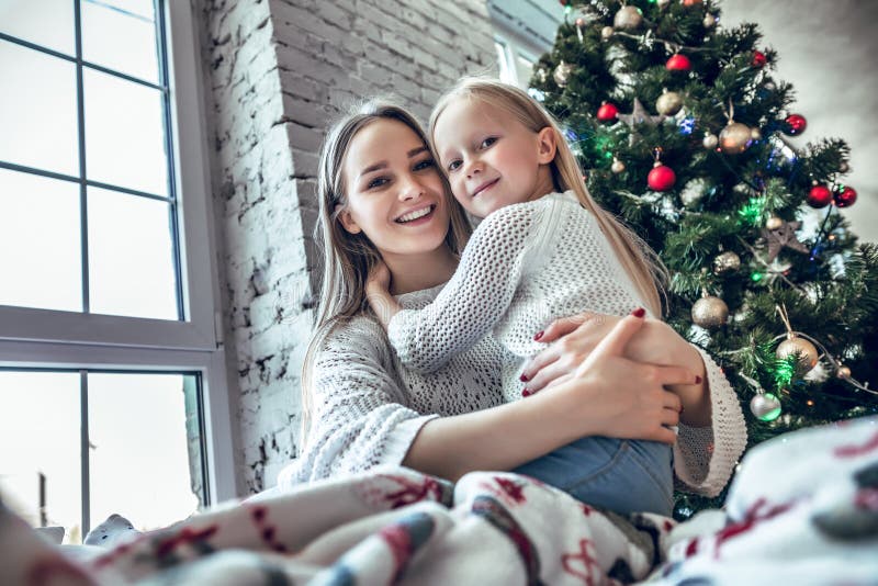 Cheerful mother and daughter sitting on the bed near beautiful decorated Christmas tree stock photos