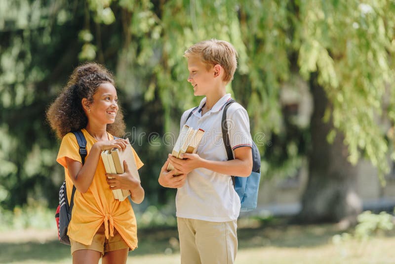 Cheerful multicultural schoolkids smiling and speaking while holding books royalty free stock photos