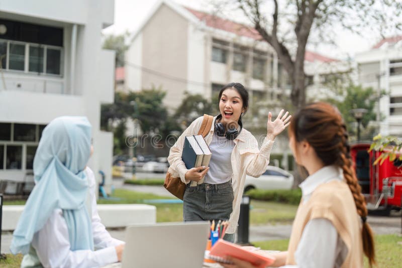 Cheerful multicultural student waving and carrying books outdoors in a university campus. stock photos