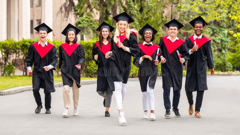 Cheerful multirasist Student i examinationskostnad som går på universitetscampus arkivbild