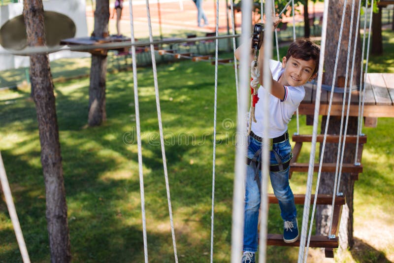 Cheerful preteen boy posing while climbing at rope park stock photo Cheerful preteen boy posing while climbing at rope park stock photo