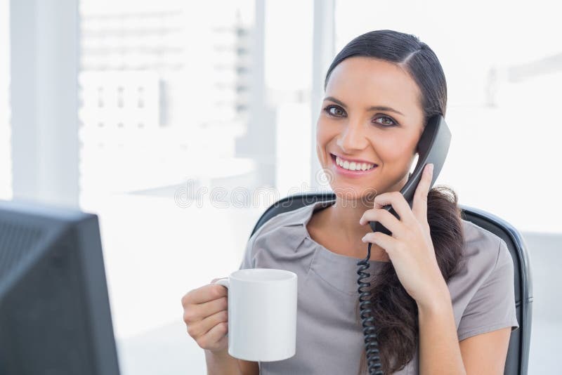 Cheerful secretary answering phone and drinking coffee royalty free stock image Cheerful secretary answering phone and drinking coffee royalty free stock image