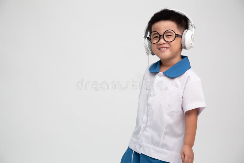 Cheerful smiling asian little boy in student uniform listening music with headphone isolated on white background.