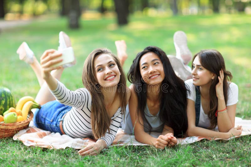 Cheerful smiling girls taking selfie lying on blanket on grass stock photography Cheerful smiling girls taking selfie lying on blanket on grass stock photography