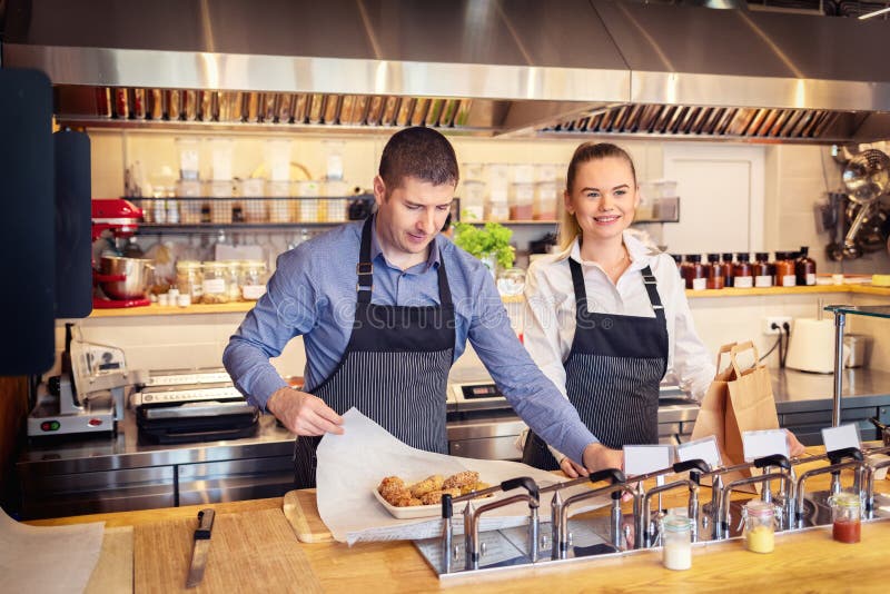 Cheerful waiter wearing apron serving takeaway food at counter in fast food restaurant