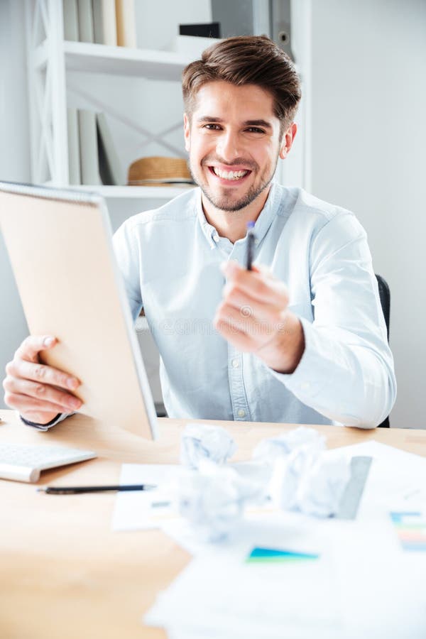 Cheerful young businessman giving notepad and pen to you.