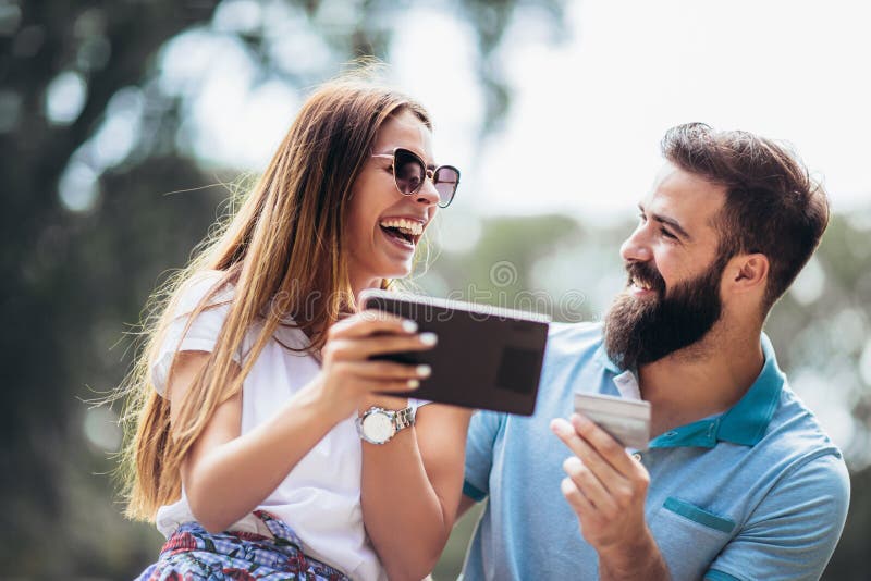 Young couple sitting on a park bench and uses a digital tablet for online shopping stock image Young couple sitting on a park bench and uses a digital tablet for online shopping stock image