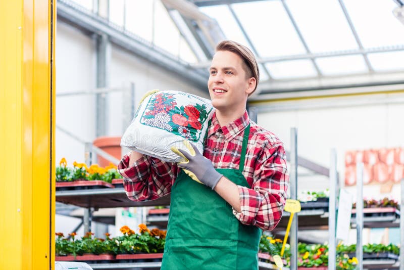 Cheerful young man carrying a bag of potting soil while working as florist