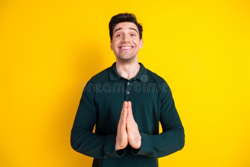 Cheerful young man clasping hands together as a gesture of gratitude or plea against a vibrant yellow background stock photo