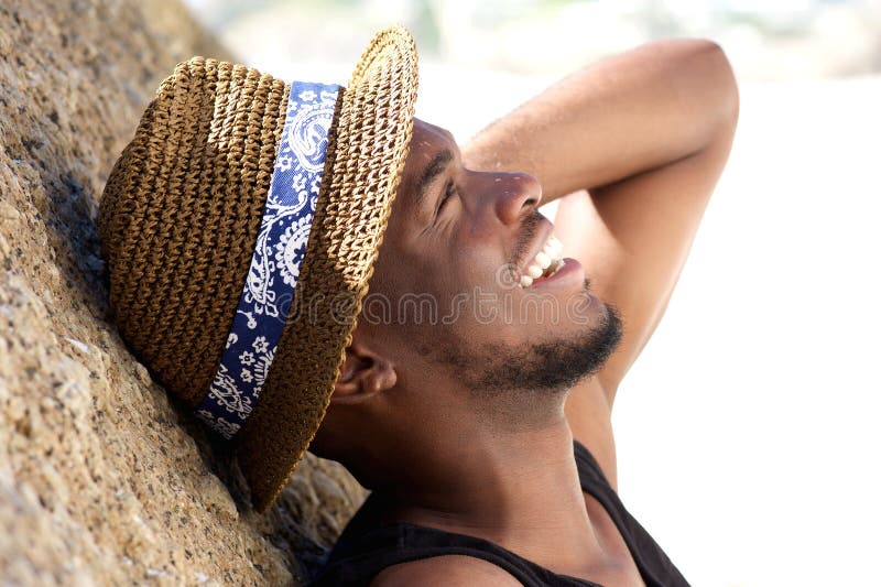 Cheerful young man laughing at the beach with hat royalty free stock image