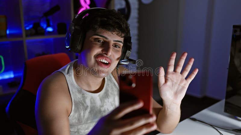 A cheerful young man streams on smartphone in a neon-lit gaming room at night stock image