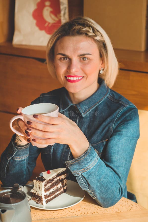 Cheerful young woman drinking warm coffee or tea enjoying it while sitting in cafe stock photo Cheerful young woman drinking warm coffee or tea enjoying it while sitting in cafe stock photo