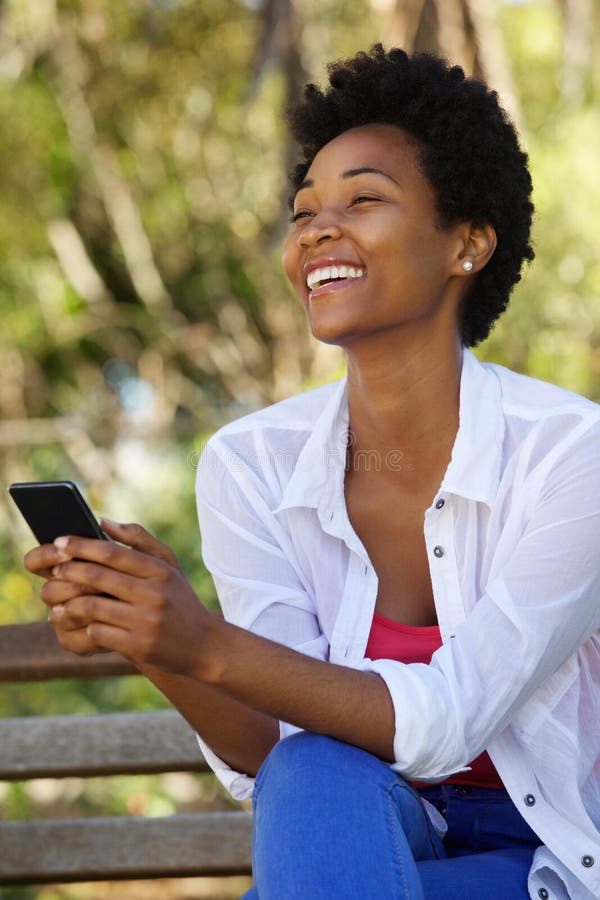 Cheerful young woman sitting on a bench with a mobile phone