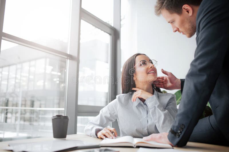 Cheerful young woman sit at table and smile to her boss. She look at him. Guy is sexually excited. He touches her face. royalty free stock images Cheerful young woman sit at table and smile to her boss. She look at him. Guy is sexually excited. He touches her face. royalty free stock images