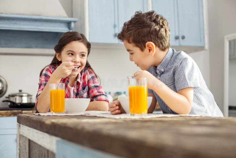 Delighted girl looking at her brother and eating