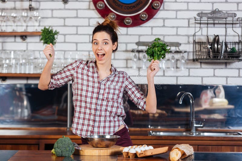 Cheerul woman holding dill and parsley on the kitchen