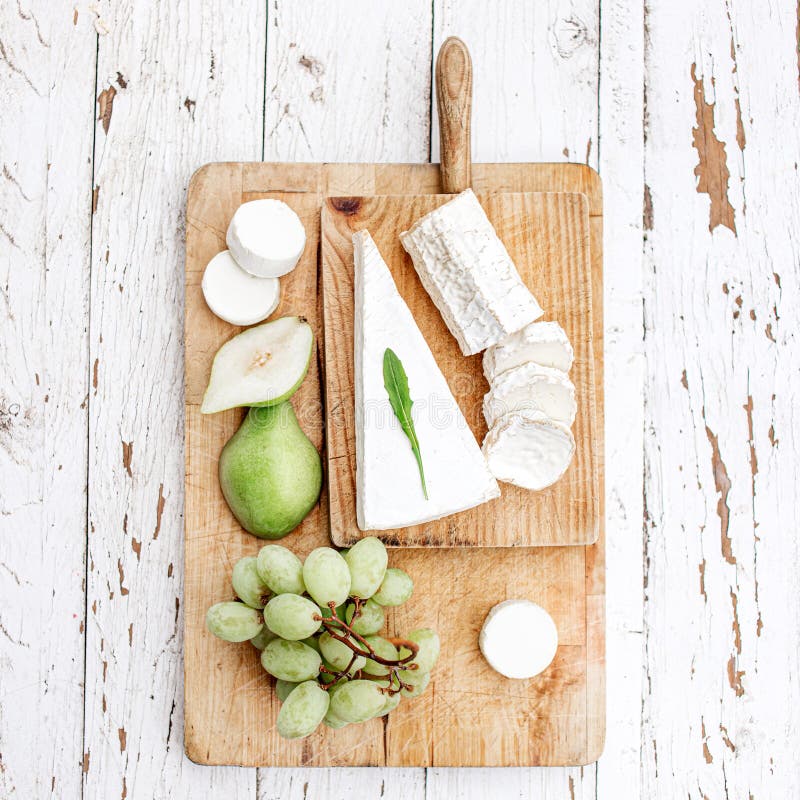 Cheese Board  with different cheese, pear and grapes on white  wooden background. Cheese platter Top view. Copy space