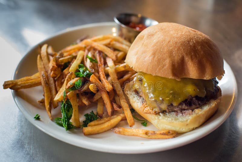 Cheese Burger and Fries with Herbs on a White Plate, Metal Table Stock
