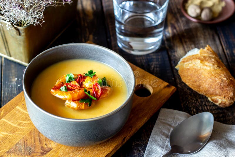 Cheese cream soup with grilled shrimp on a wooden background