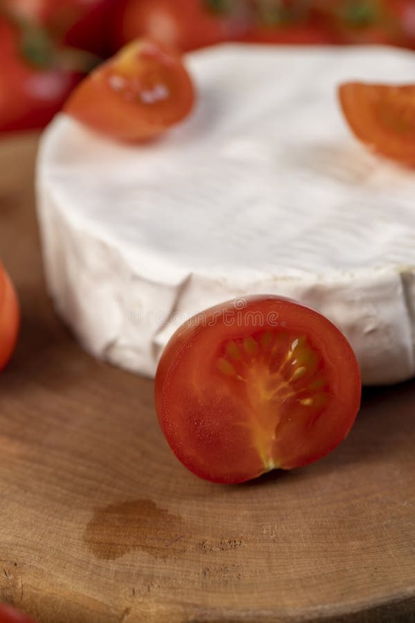 Piece of ripe soft cheese and some small red round tomatoes on the table, Focus on the tomato side view stock photography