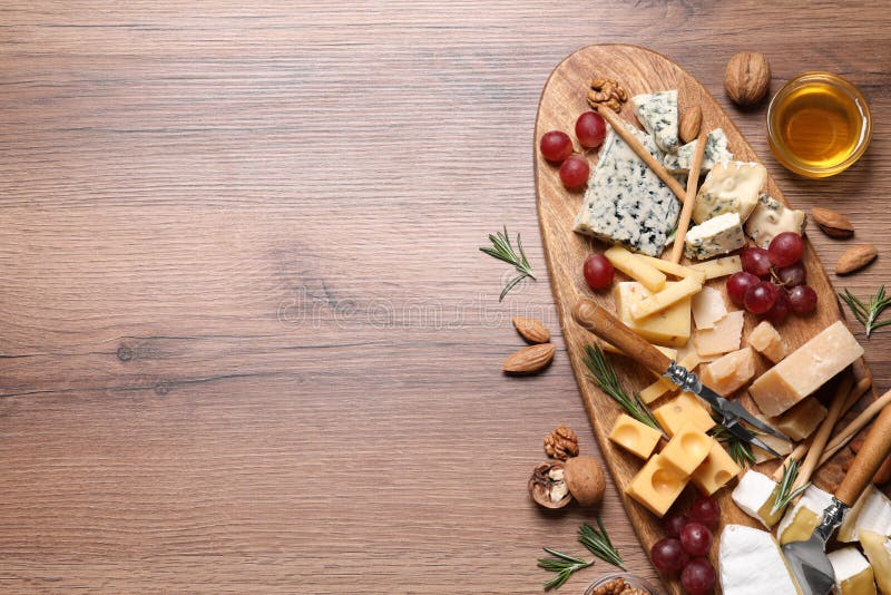 Cheese plate with honey, grapes and nuts on wooden table, flat lay. Space for text