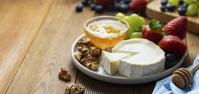 Cheese plate round sliced soft cheese, blueberry, strawberry, grapes and honey on wooden table. Banner