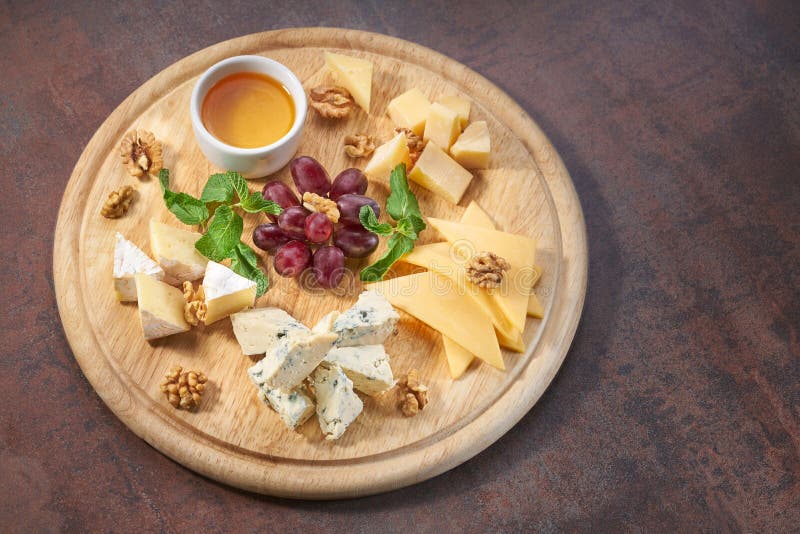 Cheese plate served with grapes, honey and nuts on a wooden background