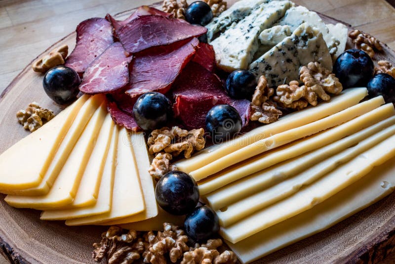 Cheese Plate with smoked meat, walnuts and grapes on wooden surface.