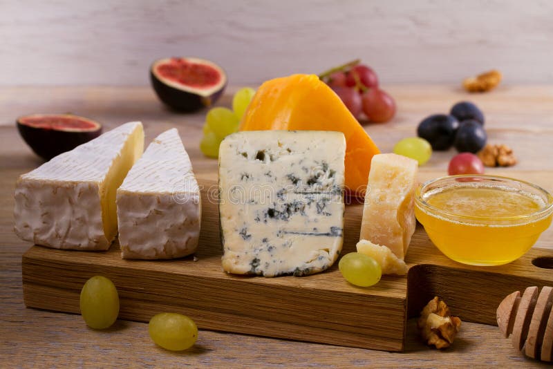 Cheese plate. Various types of cheese with grapes, honey, figs and nuts on rustic wooden table.