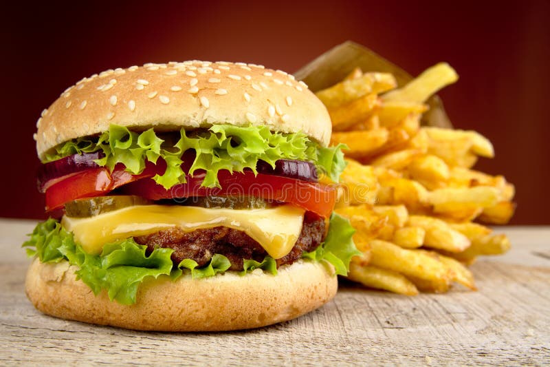 Cheeseburger en frieten op rode schijnwerper op houten lijst stock afbeelding Cheeseburger en frieten op rode schijnwerper op houten lijst stock afbeelding