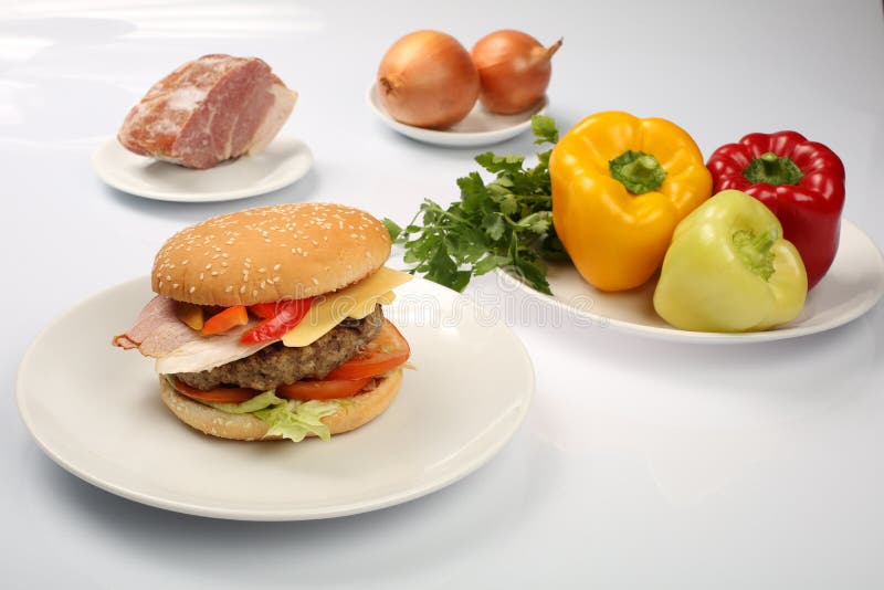 Cheeseburger с пирожком бекона и говядины на плите с овощами, болгарским перцем, томатами, луками, огурцом, петрушкой и салатом н стоковые фото Cheeseburger с пирожком бекона и говядины на плите с овощами, болгарским перцем, томатами, луками, огурцом, петрушкой и салатом н стоковые фото